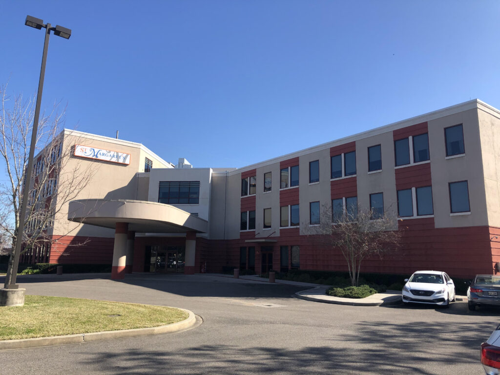 A medical building with a large drive-up area, made of pink brick and red siding. A sign on the front says "St. Margaret's".