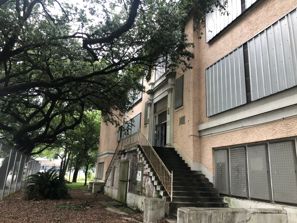 A stairway leads up to a door in a pink building surrounded by trees.